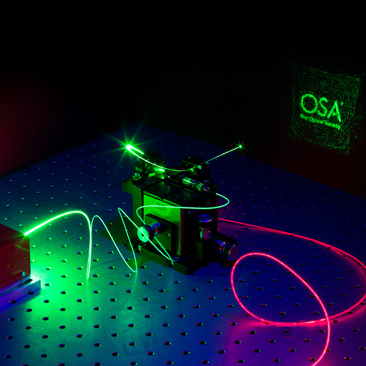 This image shows a number of optical phenomena, starting with a green laser (532-nm Nd:YAG) guided by a multimode silica optical fiber to a vial containing an organic dye